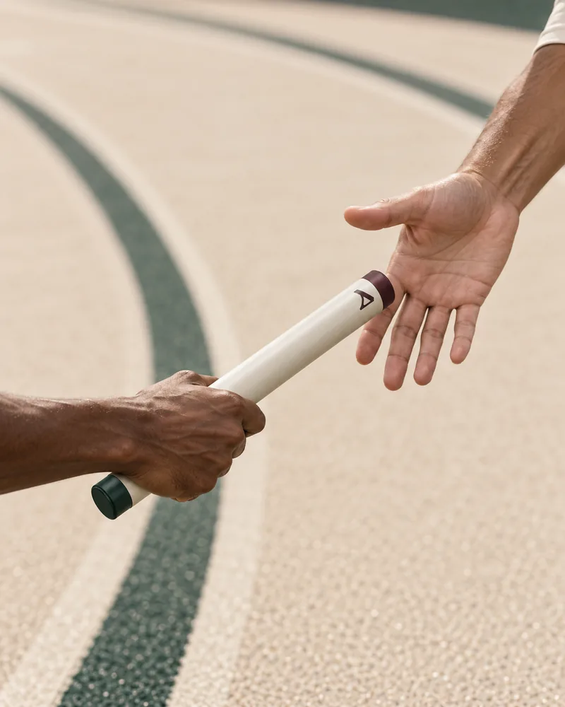 Two runners passing a cream relay baton, with evergreen lanes in the background.